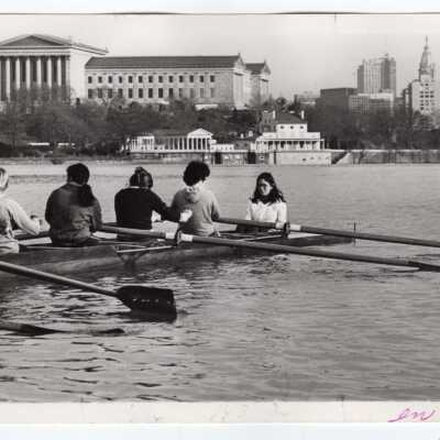 Women's crew/rowing team practicing on Schuylkill River with Boathouse Row and Philadelphia Museum of Art in background.