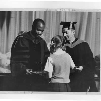 Young girl presenting gift to Francois Tombalbaye, President of Chad, during convocation, October 26, 1970 with Terrence Toland, S.J., looking on.