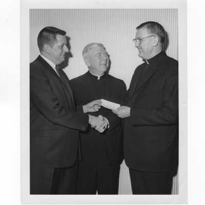 William F. Maloney, S.J., receiving check from alumni association officer with Lawrence McHugh, S.J. watching, January 18, 1965.