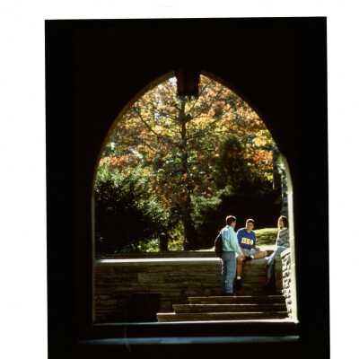 Exterior view from Barbelin archway of three students sitting on wall talking in the fall.