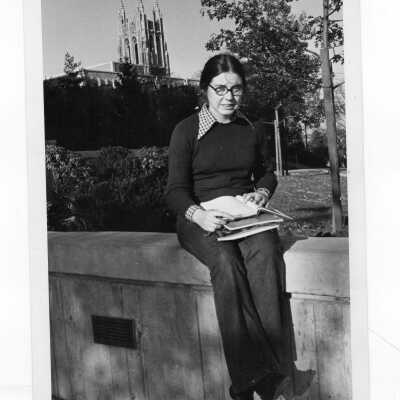 Woman student sitting outside on wall with Drexel Library and Barbelin Tower in distance.