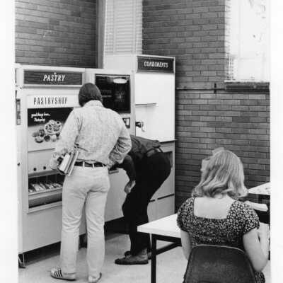 Students in lounge area buying food from pastry and condiments vending machines.