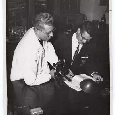 Biology professor, Mark Bauer, S.J., working with student at microscope in science laboratory, c. 1955.