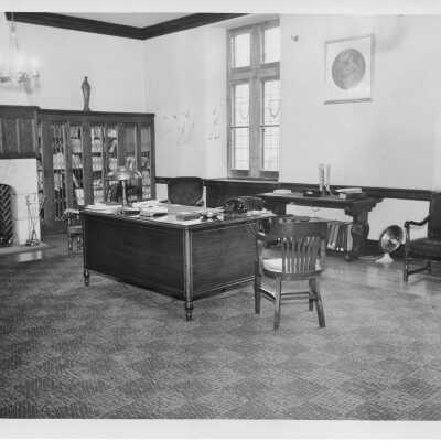 Interior view of Dean's office in Barbelin with fireplace, bookcases with leaded glass doors, desk, and chairs.