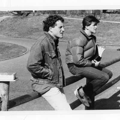 Two male students sitting on wooden fence near track in winter.