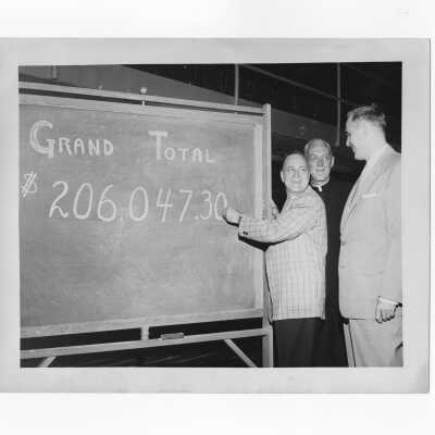 J. Joseph Bluett, S.J., and Robert Cranage and Ray Trainer of the alumni association check total funds raised on blackboard during fundraising drive, 1959.