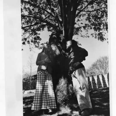 Two students standing and talking under large shade tree.