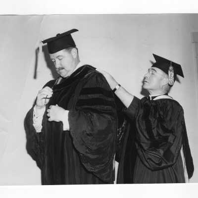 Honorary Degree recipient, Thomas F. Murphy being helped with academic robe by John J. Long, S.J. at 1950 graduation/commencement ceremony.