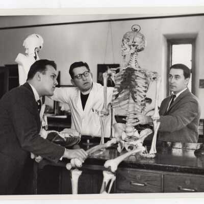 Biology professor Francis J. MacEntee, S.J., with two students in science laboratory looking at skeleton, April 1964.