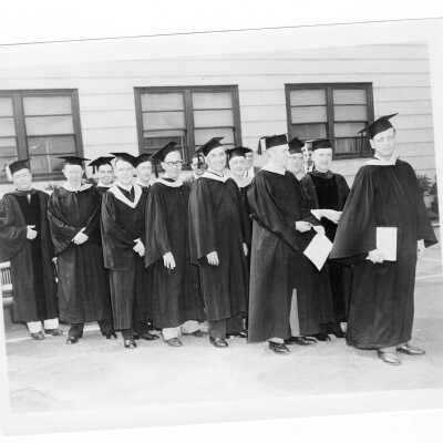 Members of the class of 1933 in cap and gown standing in front of Cardboard College prior to ceremony marking their twenty-fifth anniversary during 1958 graduation/commencement.
