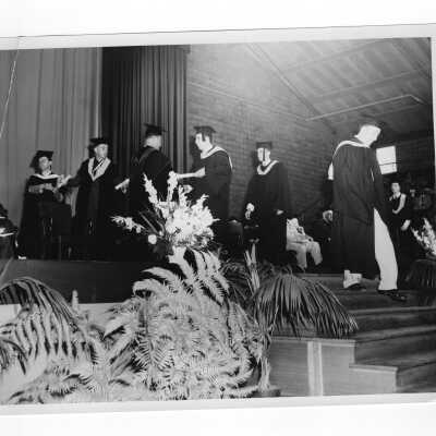 Edward G. Jacklin, S.J., and Michael Boland handing out diplomas to graduates during 1955 graduation/commencement ceremony.