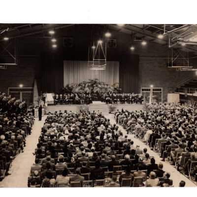 View of individuals seated on podium for dedication of Field House (Sports Complex) with John J. Long, S.J., U.S. Senator Frank Meyers (SJC graduate), Thomas Love, S.J., General Frank Howley [ related to librarian Mary Howley]