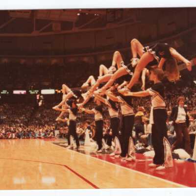 Men and women cheerleaders at basketball game performing routine.
