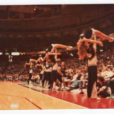 Men and women cheerleaders at basketball game performing routine.
