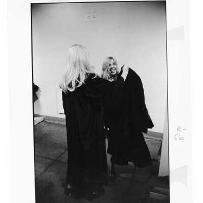 Two women graduates putting on cap and gown during 1971 graduation/commencement.