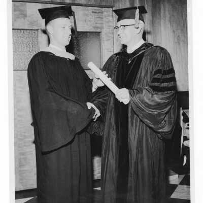 Graduating student receiving congratulations from his alumnus father (?) during 1956 graduation/commencement ceremony.