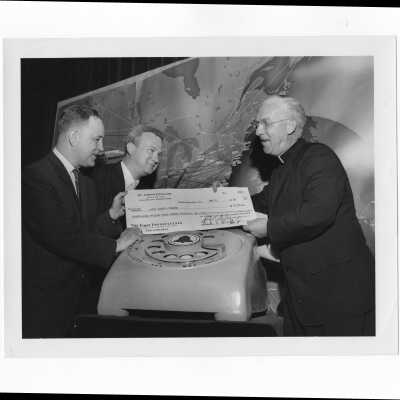 J. Joseph Bluett, S.J., receiving fundraising check from members of alumni association, Robert Cranage and Frank X. Duff.