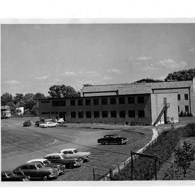 View of veterans barracks used as residence hall from parking lot with cars. Located near Cardboard College also known as Barbelin Annex.