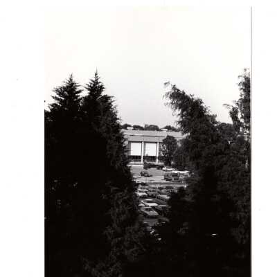 Distant view of Sports Complex and cars in parking lot through trees.
