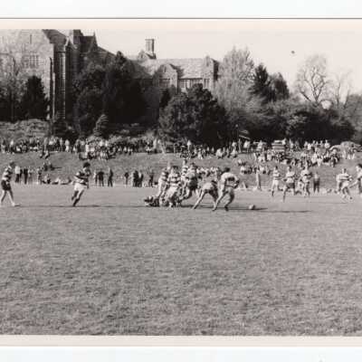 Men's rugby game on Finnesey Field with Barbelin Hall in background.