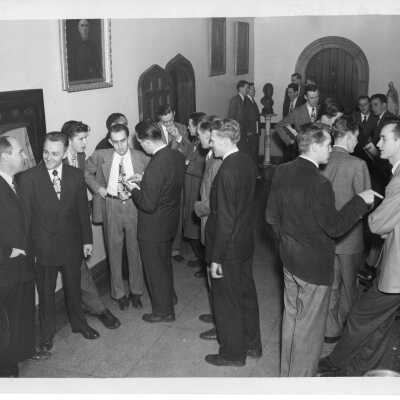 Interior of hallway in Barbelin building with approximately twenty students talking and one smoking cigarette.