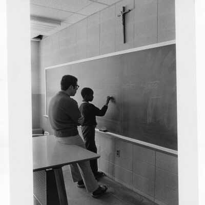 Student tutoring child in mathematics standing at blackboard as part of community service/outreach project.