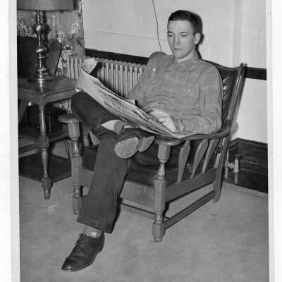 Student resident of Quirk Hall reading newspaper in living room.