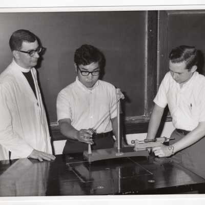 Physics professor, Howard Heim, S.J., working in laboratory with two high school students, 1970.