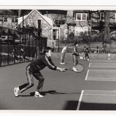 Men's tennis match with Barry Annex in background.