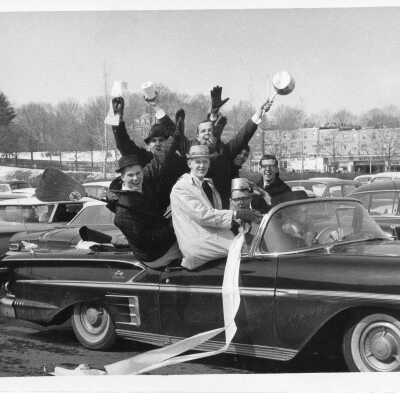 Students in booster club riding in convertible automobile with toilet paper streamers as part of pep rally.