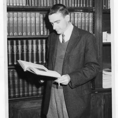 Student resident of Quirk Hall standing in front of bookshelf smoking cigarette.