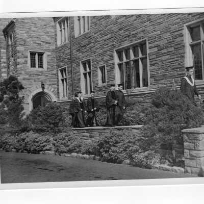 Faculty members in cap and gown walking in front of Barbelin to graduation commencement ceremony in quadrangle. Joseph Hogan, S.J. at center.