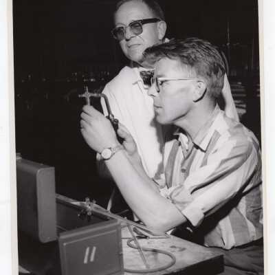Chemistry professor with graduate student in science laboratory, c. 1960, possibly using glass blowing equipment.