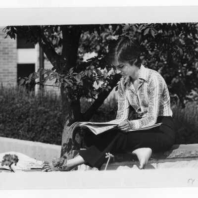 Woman student reading newspaper on wall in front of Drexel Library in spring.