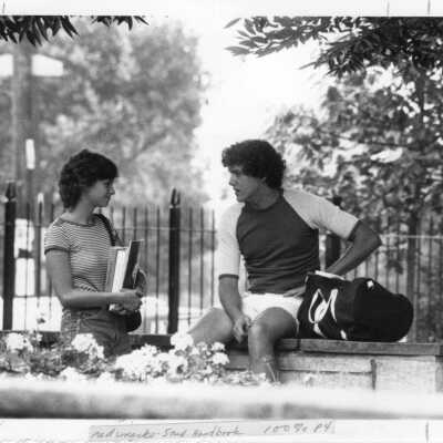 Two students talking alongside wall in spring.