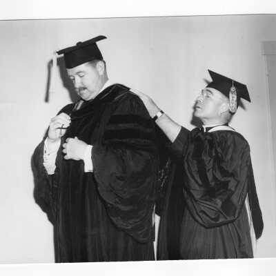 Honorary Degree recipient, Thomas F. Murphy being helped with academic robe by John J. Long, S.J. at 1950 graduation/commencement ceremony.