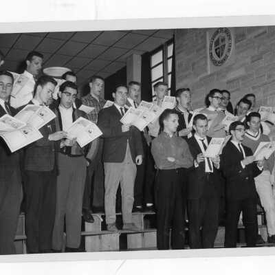 Students in Glee Club practicing in street clothes and holding sheet music.