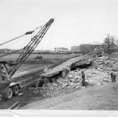 Finnesey Field preparation with crane destroying stands with Field House and Cardboard College in background.