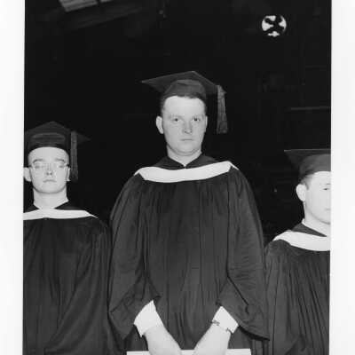 View of Stephen J. McEwen, honor student and other graduates during 1954 graduation/commencement ceremony in Field House. Fan shown in background.