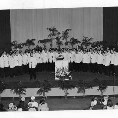 Members of Glee Club wearing white tuxedos giving concert in Flanigan Auditorium.