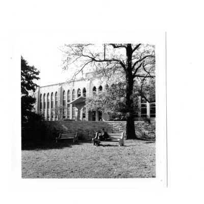 Exterior front view of Drexel Library with student sitting on bench in front of stone wall.