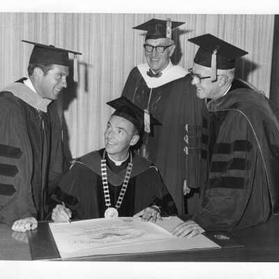 Terrence Toland, S.J., signing honorary degree with John R. Bunting, Gaylord P. Harnwell, and Mayor James H.J. Tate watching during September 1969 graduation/commencement.