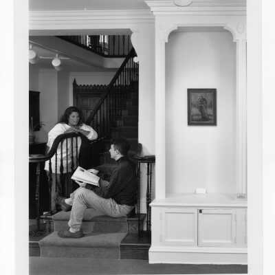 Photograph of painting of "Patron Saint of the New World" exhibit in Boland Hall with two students near stairwell talking.