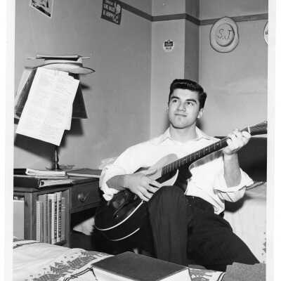 Student resident of Quirk Hall playing guitar in dormitory room.