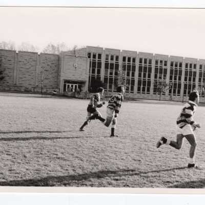 Men's rugby game with Post Hall (formerly Villiger) in background.