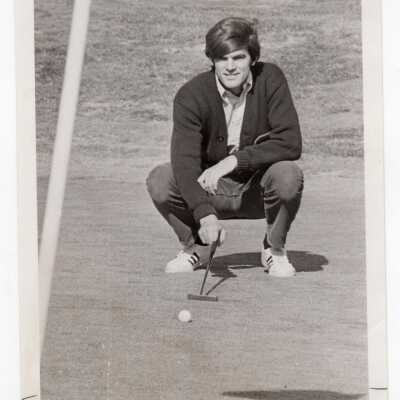 Men's golf team member lining up putt.