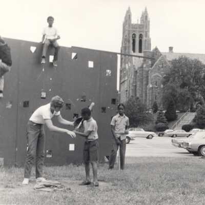 Student playing baseball with neighborhood children on SJU campus as part of community service/outreach program during summer.
