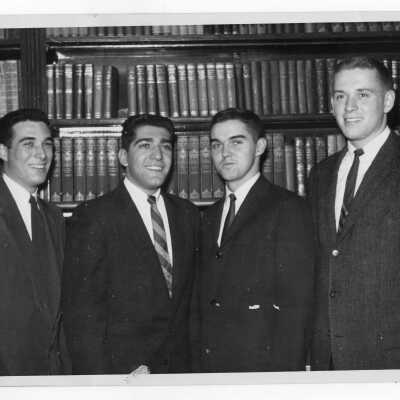Four student residents of Quirk Hall standing in front of bookshelves.