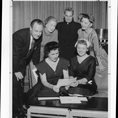 Michael Smith, S.J., and member of alumni association with several wives of alumni associaiton members planning an event, January 5, 1958.
