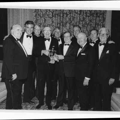 Donald I. MacLean, S.J., and alumni standing with recipient of 1983 Shield of Loyola Award, Paul E. Kelly, class of 1934. Alumni include J. Gallagher, M. Kempski, C. Brennan, A. Tegler, F. Wellock, and Honorable William Cahill.